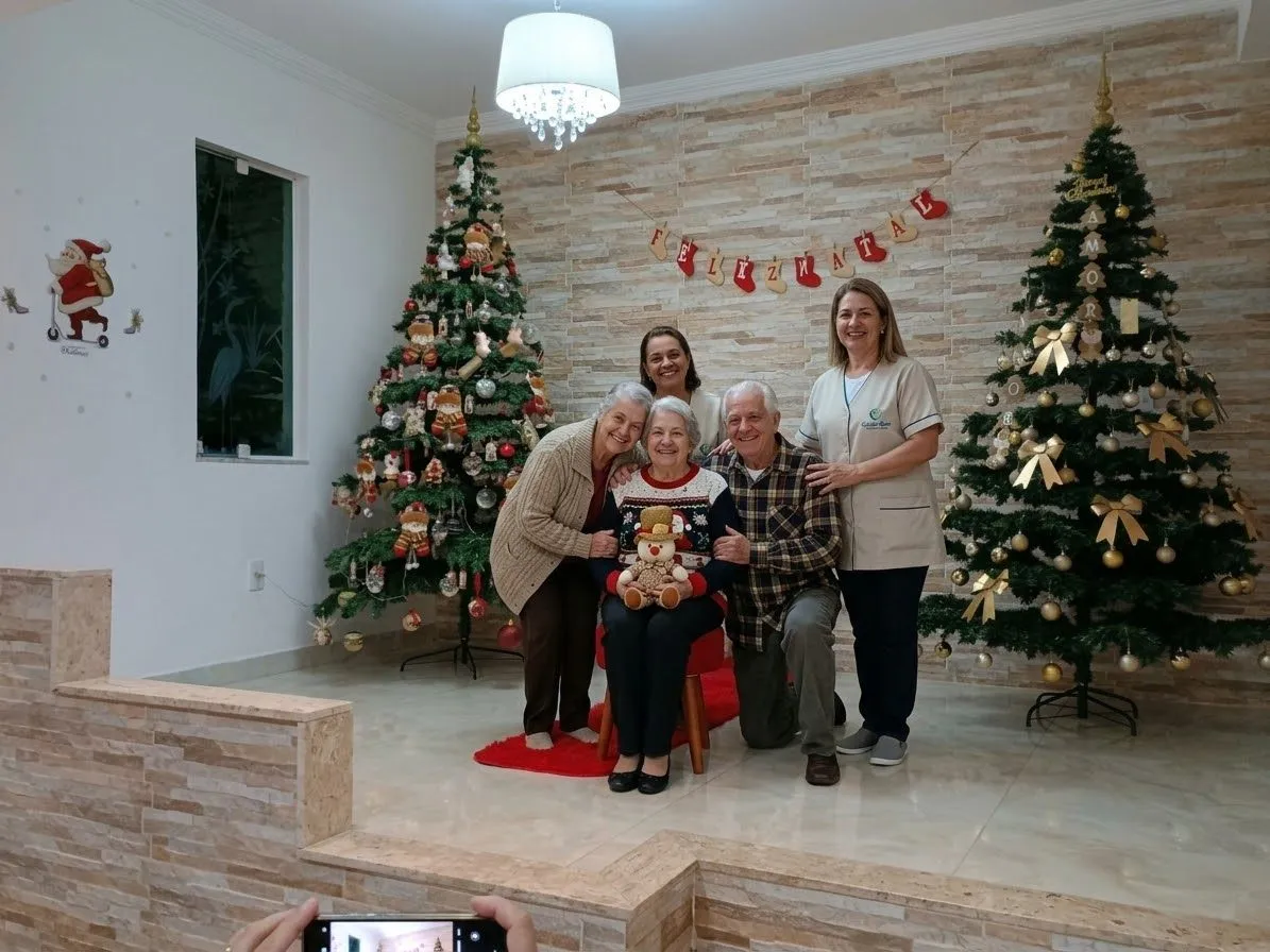 Idosos e cuidadoras juntos ao lado das árvores de Natal